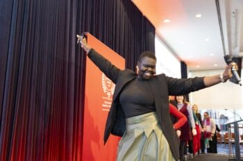 A speaker posing on stage in the Melbourne Symposium
